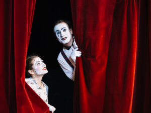 smiling-female-mime-artist-looking-at-male-mime-artist-peeking-from-curtain